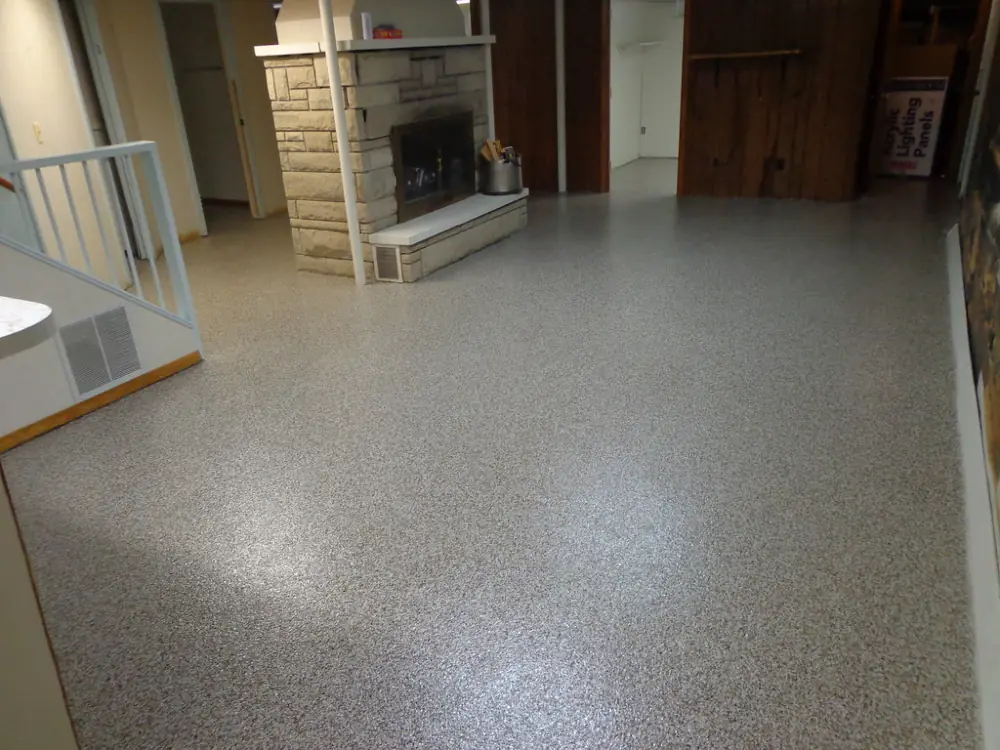 A finished basement with a flake floor, a stone fireplace and stairs.