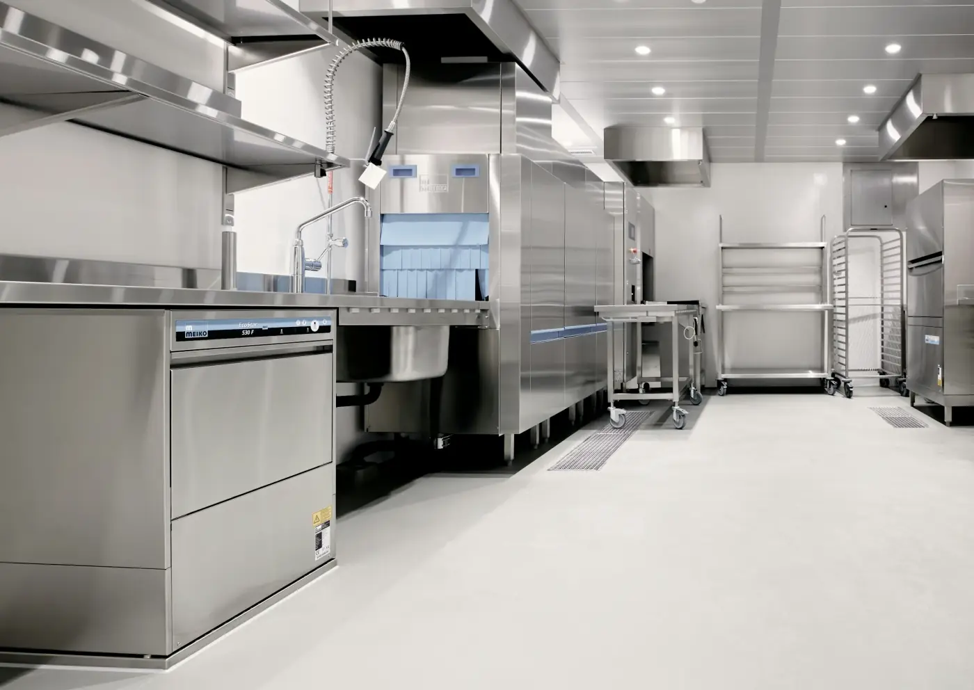 A commercial kitchen with stainless steel equipment and a light seamless floor.