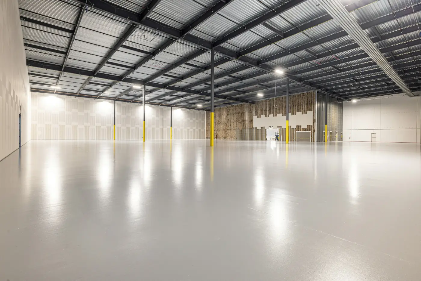An empty warehouse with a light, glossy coated concrete floor under rows of lights.